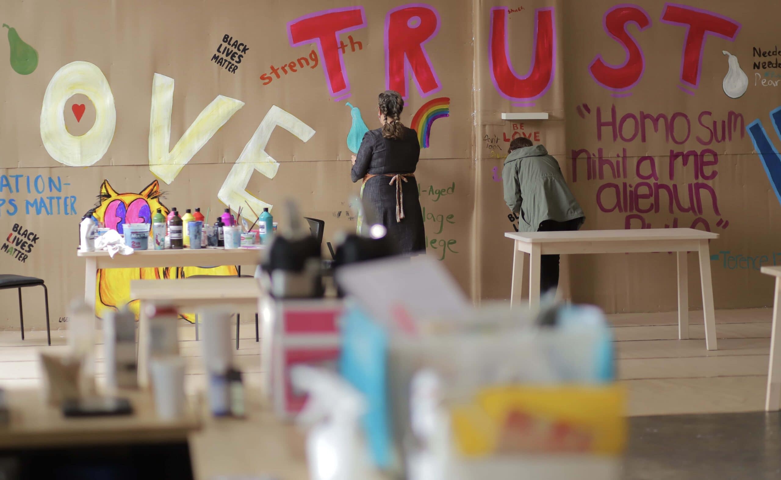 Mural artists painting LOVE and TRUST on a wall.